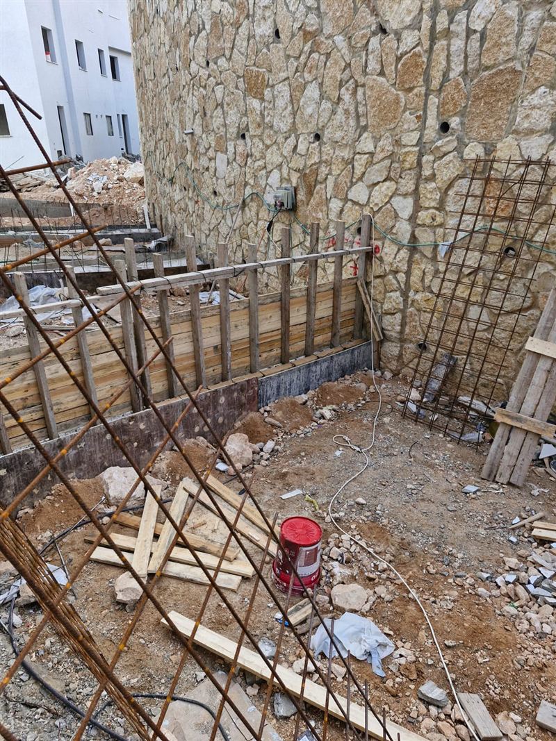 תבניות עץ ליציקה לצד קיר אבן, בשלב העבודות בשטח